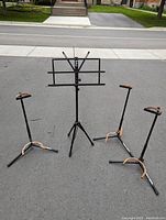 Photo showing two black metal guitar stands with rubber padding beginning to age and crack, alongside one black adjustable music sheet stand with tripod base.