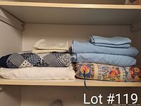 Photo of folded queen sheet set, two quilt comforters and assorted pillowcases on shelf.
