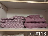 Two sets of folded queen sized sheets on a shelf, one patterned purple and white set on the left and one solid purple striped set on the right.