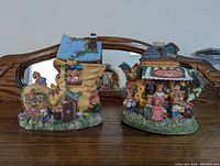 Two fairy tale themed coin banks next to each other on a wooden surface, showing detailed painted designs and characters around them