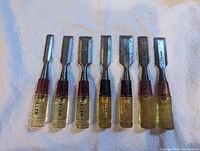 Photo showing all seven Fuller professional scrapers arranged side by side to display blade and handle variations.