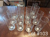 Photo showing 13 tall clear glass cylinder vases arranged on a wooden surface, all identical in shape and size, transparent glass with no decorations.