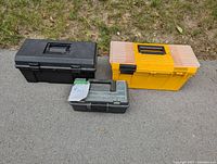 Photo showing three tool boxes in black, yellow, and green colors on pavement with grass background.