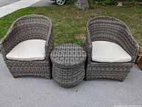 Front view of two resin wicker armchairs with beige cushions flanking round storage table.