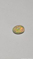 Oval natural Ethiopian opal cabochon gemstone showing rolling multicolor flashes on grey background.