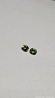 Two small oval cut multicolored sapphires on a white background showing yellow-green, teal, and blue tones.