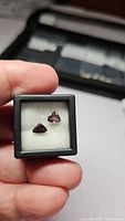 Two small triangular untreated Tanzanian sapphires placed on white cushioned background in black display box, showing deep red and purple pink colors.