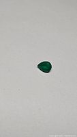 Image showing the vivid lime green pear-cut green onyx gemstone from a distance on white surface