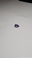 Pear-shaped purple amethyst gemstone placed on a white surface showing its size and faceting
