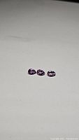 Three pear cut amethyst gemstones with purple color placed on a white background showing their shape and clarity.