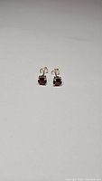 Pair of small square cushion-cut cherry red garnet stud earrings with 925 sterling silver four-prong settings shown on a plain background.