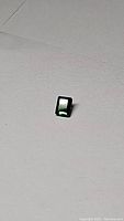 Rectangular fluorescent electric green tourmaline gemstone shown from an angle on a white background, highlighting its bright color and clarity.