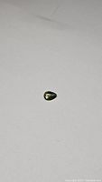 Pear cut green sapphire gemstone on white background showing size and vibrant green color.