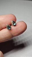 Close-up image of a pair of teardrop-shaped labradorite earrings held on fingers showing the iridescent flash of the stones and scalloped sterling silver setting.