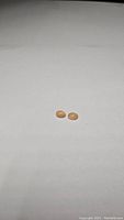 Two small oval peach moonstone cabochons placed on a plain white background, showing smooth polished surfaces and soft peach color.