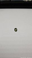Photo of a single oval cut bright green sapphire gemstone on a white background, showing size and color.