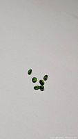 Six small oval cut green gemstones scattered on a white background, showing rich green color and transparent clarity.