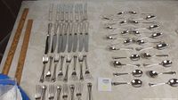 Overview of cutlery laid flat showing knives, forks, tablespoons, and teaspoons with ruler for scale