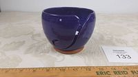 Front and side view of deep blue ceramic yarn bowl with swirl cut-out and natural clay base, showing shape and glaze.