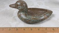 Side view of carved stone bird with ruler showing approximate length of 8 inches.