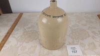 Front view of beige stoneware jug with 'WM. Radam's Microbe Killer' text, showing the full body and neck, on a floral tablecloth with a measuring ruler nearby.