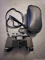 Front view of Carl Wetzlar Micro Executive binoculars with strap and carrying case on a dark surface.