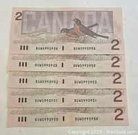 Front sides of five Canadian two-dollar bills with serial numbers visible showing sequential order.
