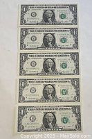 Five sequential 2009 US one dollar bills laid out showing front side with serial numbers from B01590911A to B01590915A.