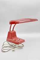 Side view of red vintage desk lamp showing cord, base, and rectangular shade with visible wear