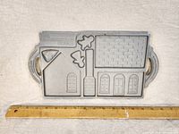Front view of vintage cast iron baking mold in the shape of The Gingerbread House with clear structural and decorative details and integrated handles.