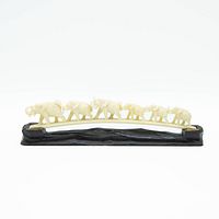 Front view of the vintage ivory-colored carved elephant figurines arranged in a line on a black carved wooden base.