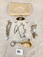Photo showing all items flat on cloth background for overview: small beaded purse, floral enamel compact, silver-tone earrings, chain bracelet with heart charm, cameo brooch, wire puzzle, fur keychain.