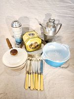 Photo showing a variety of vintage kitchenware items including Pyrex bowl, knives, metal pitcher, ceramic pot, tin, and stacked containers.