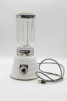 Front view of vintage Osterizer Deluxe blender with beehive glass jar, dial, cord, and plug visible.