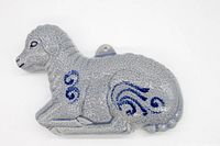 Full view showing the textured gray ceramic lamb mold with blue swirl decoration on the side and a hook at the back for hanging.