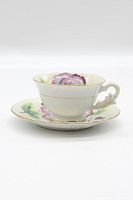 Full view of vintage ceramic teacup on matching saucer showing floral pattern and gold trim.