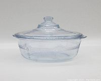 Side view of the vintage clear glass casserole dish with lid showing embossed grapevine and leaf pattern on both lid and dish.