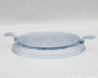 Photo of a round vintage glass serving tray with two handles and decorative pressed pattern on the surface.
