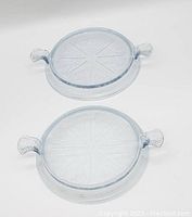 Two round clear glass serving trays each with decorative etched patterns and molded handles visible from top view.