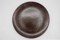 Top-down view of a vintage hammered metal plate showing textured surface and dark brown finish.