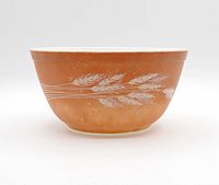 Photo shows a medium-sized vintage Pyrex mixing bowl with a brown exterior and white wheat stalk design. The bowl displays light wear marks indicating vintage use.