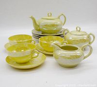Front view of the entire vintage yellow ceramic tea set showing teapot, sugar bowl, creamer, four cups and four saucers, on a white background.
