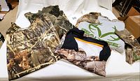 Four camouflage men's shirts arranged flat on a white cloth showcasing different styles and camo patterns.