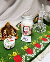 Lot displayed on green woven table runner with candle designs; items include nativity ceramic figurine, glass jar candle, Lefton trinket box and clear plastic angel tree topper.