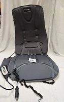 Black massage seat cushion laid out showing full design and attached cables with hand controller and car adapter plug