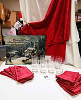Photo showing damask crimson tablecloth, 10 matching napkins, 8 clear water glasses, and Thomas Kincade fiber optic wall tapestry.