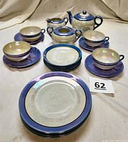 22-piece vintage blue lusterware tea set, including teapot, creamer, sugar bowl, cups, saucers, and plates arranged on beige background.