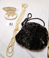 Photo showing pearl clip earrings in cream clamshell case, long cultured pearl necklace, and black velvet drawstring clutch with floral paisley pattern