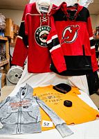 Five NHL apparel and memorabilia items including Flyers Stanley Cup Final T-shirt, Flyers zip hoodie, Devils hoodie, Wild jersey, Flyers knit hat and puck