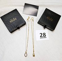 Two Slide Jewels necklaces in original black boxes with branding visible, placed on a white background.